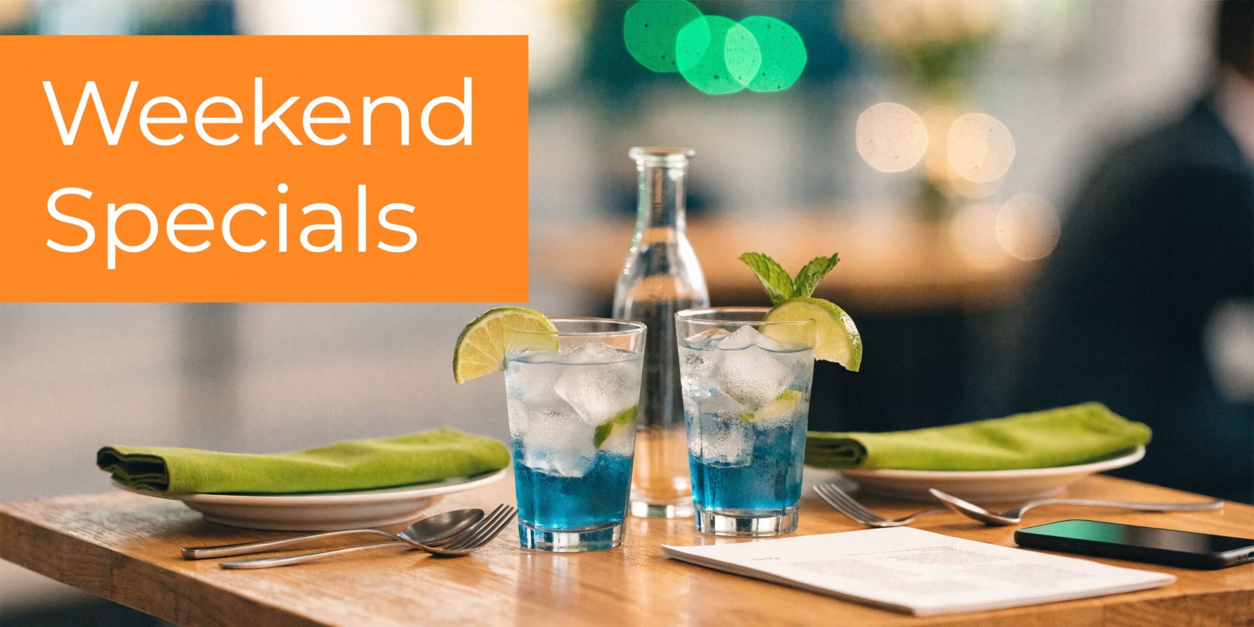 Two blue cocktails with lime and mint on a restaurant table with napkins and a menu.