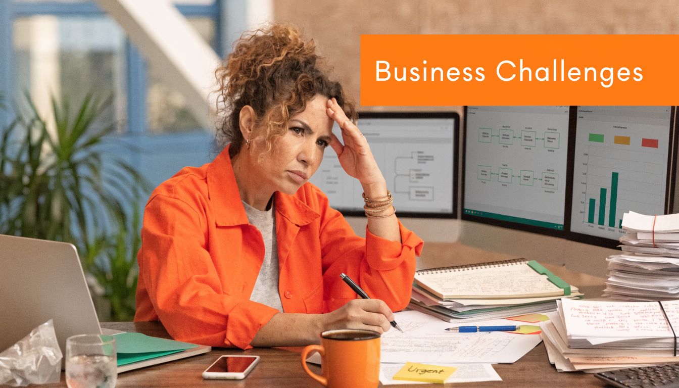 A woman sits at her desk, looking stressed and overwhelmed while working on business paperwork.