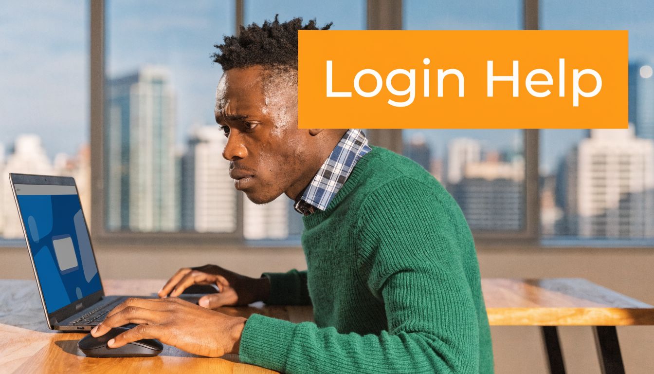 A man wearing a green sweater using a laptop at a desk with a city view.
