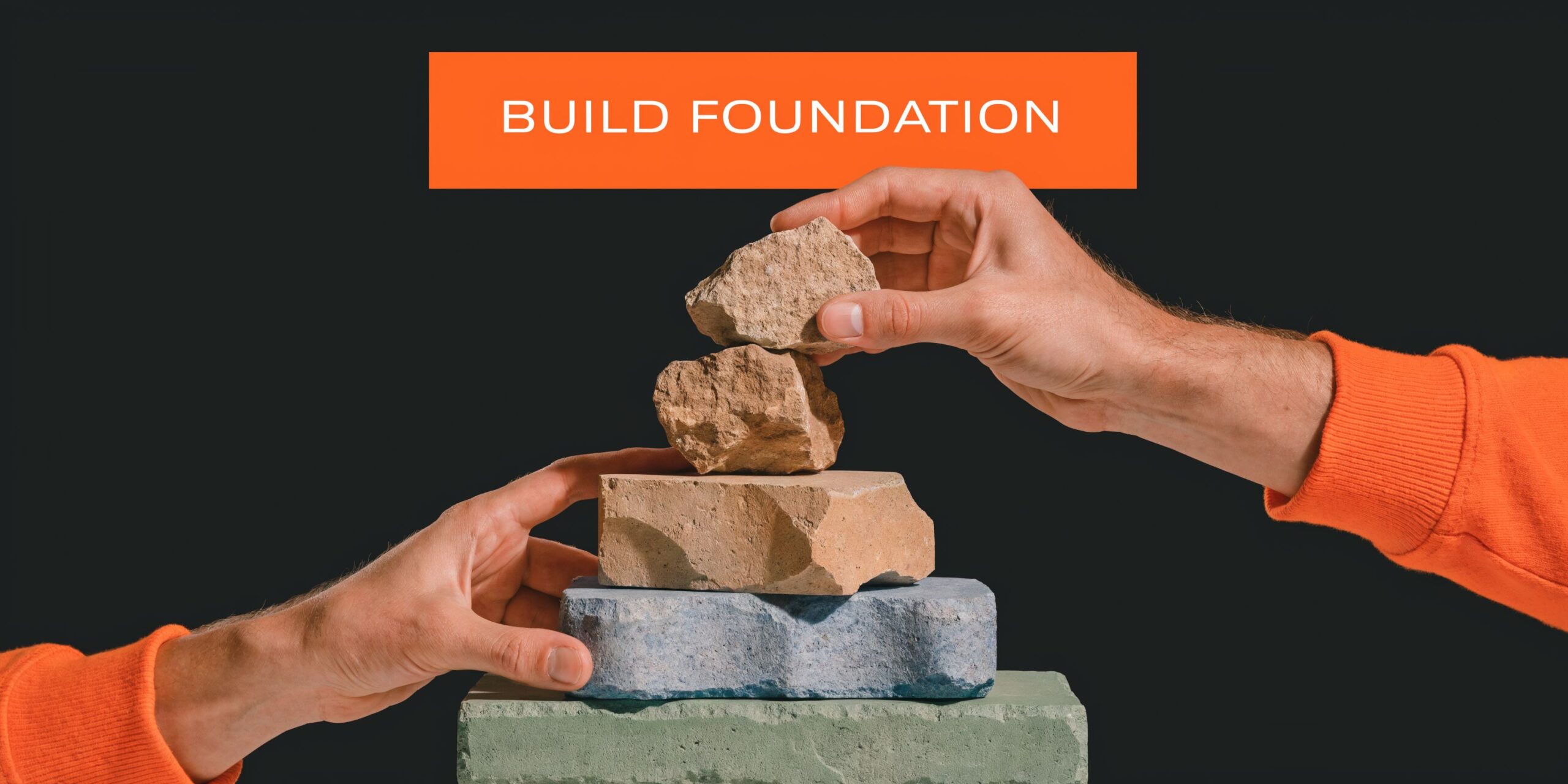 Two hands carefully stacking natural stone pieces to build a balanced tower against a dark background.
