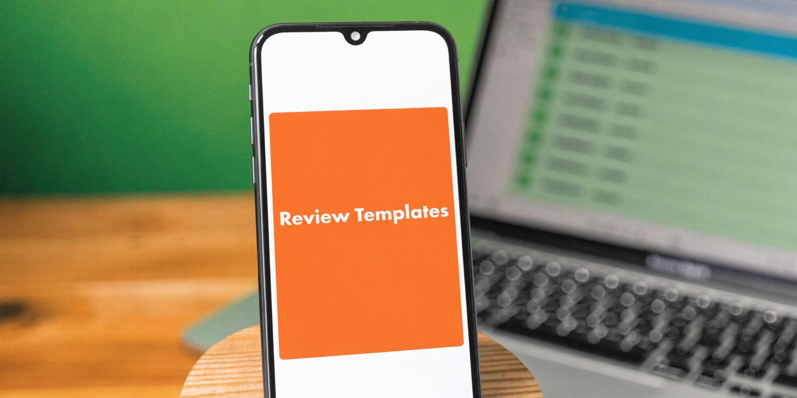 A smartphone screen displaying a bright orange square with the text Review Templates, set on a desk.