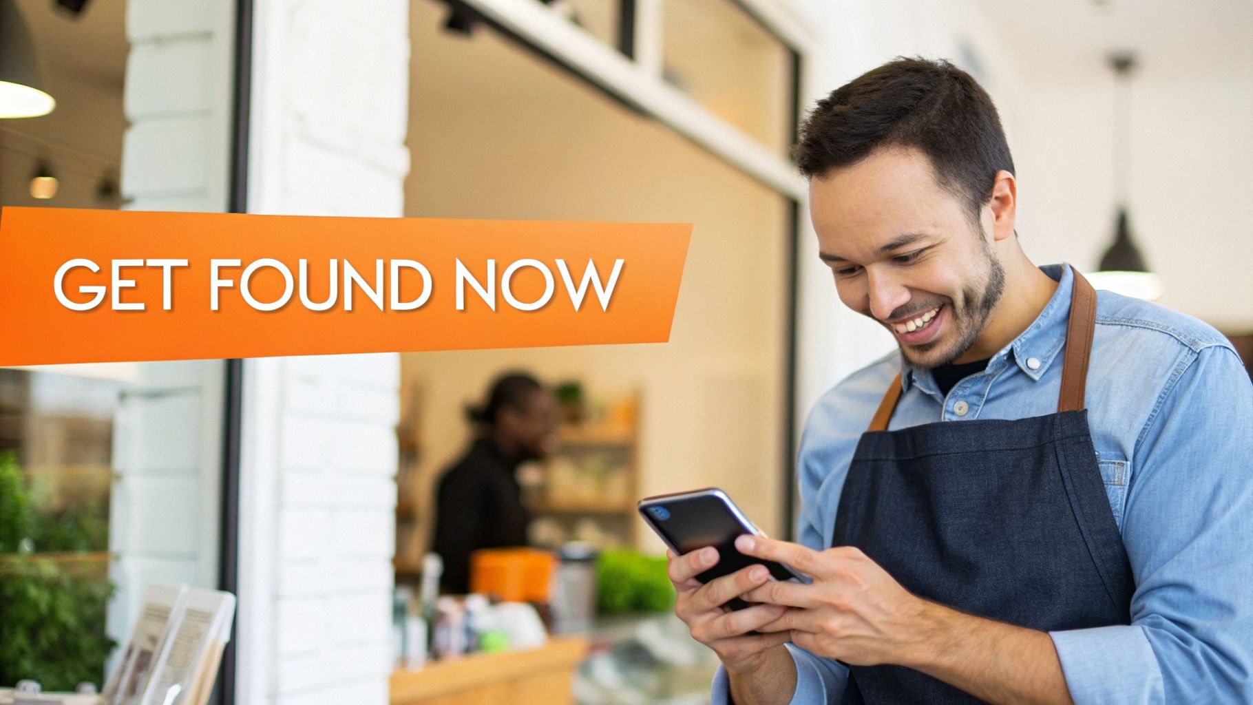 A smiling small business owner in an apron uses his smartphone in a shop.