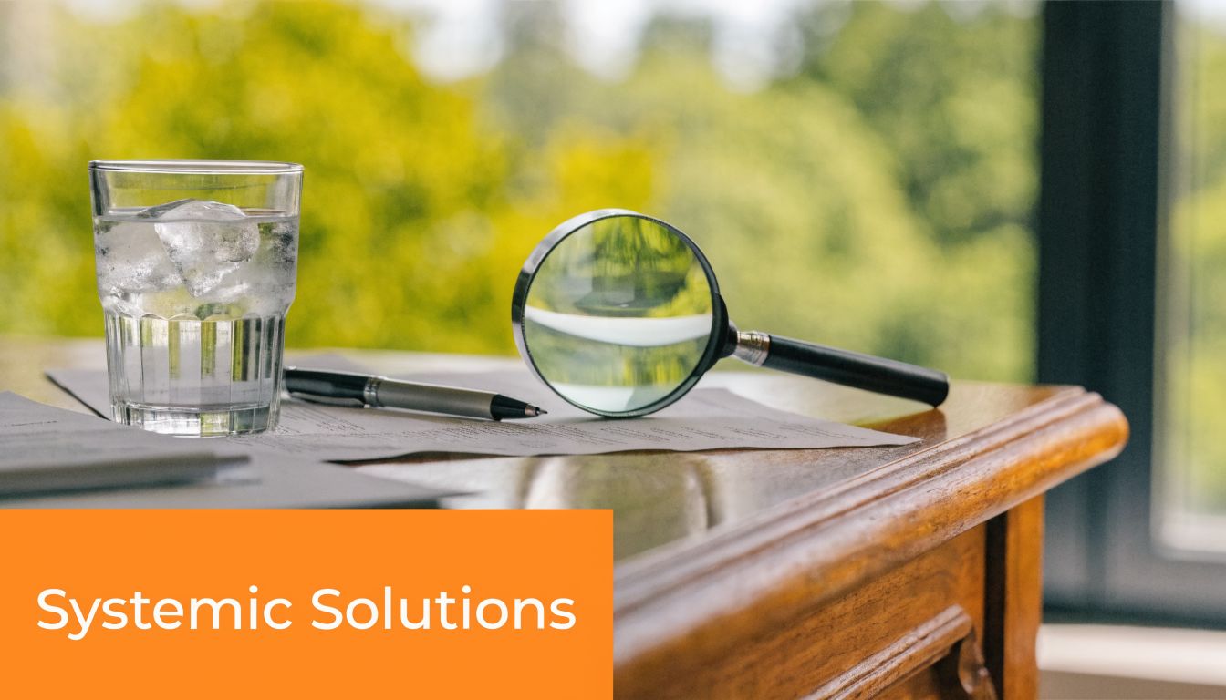 A glass of water with ice, a pen, and a magnifying glass resting on documents on a table.